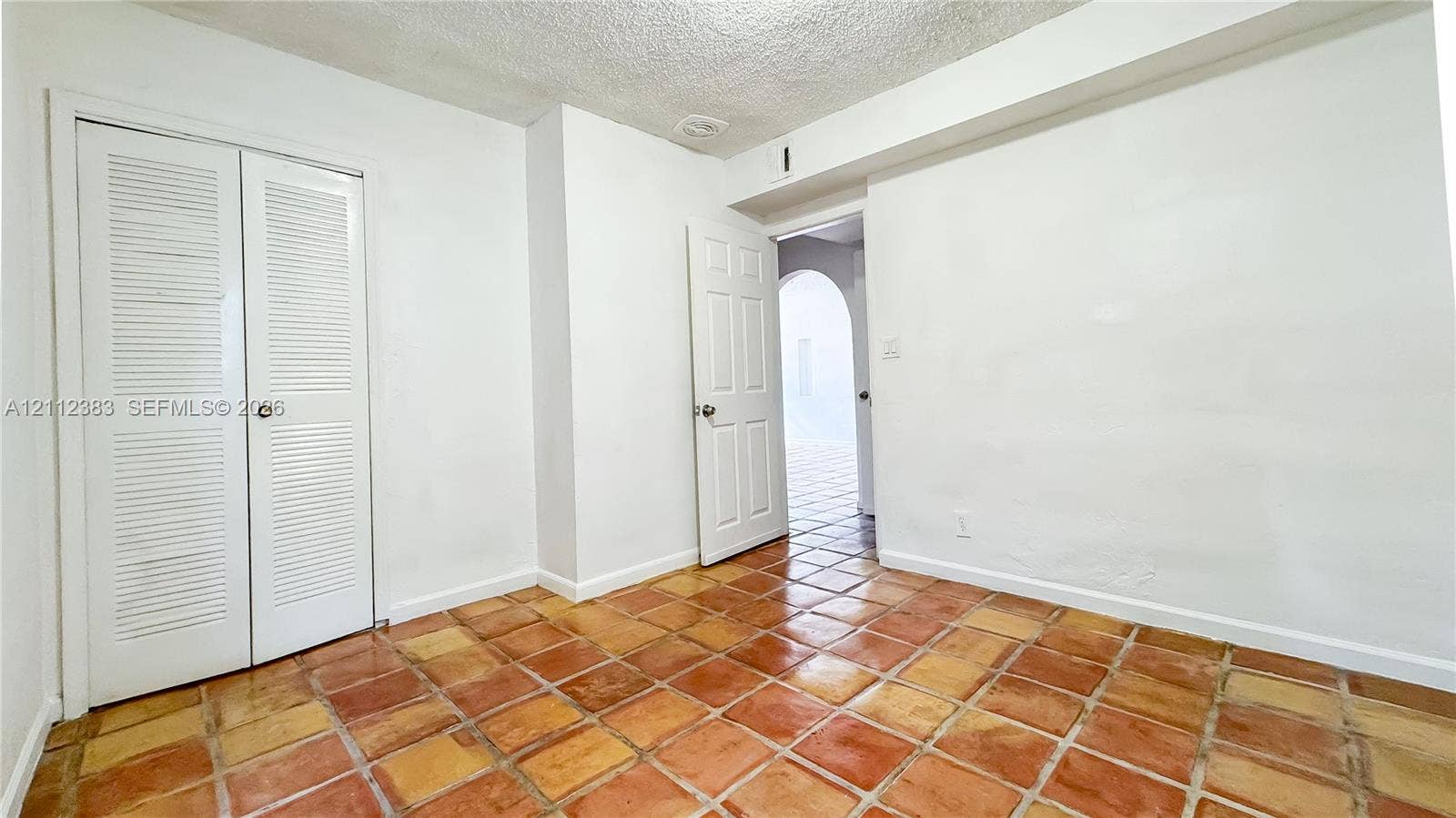 5319 Lake Boulevard, Delray Beach, Delray Beach, FL 33484 Interior space featuring terracotta-style tile flooring, double louvered closet doors, and a paneled interior door with an arched entryway visible beyond