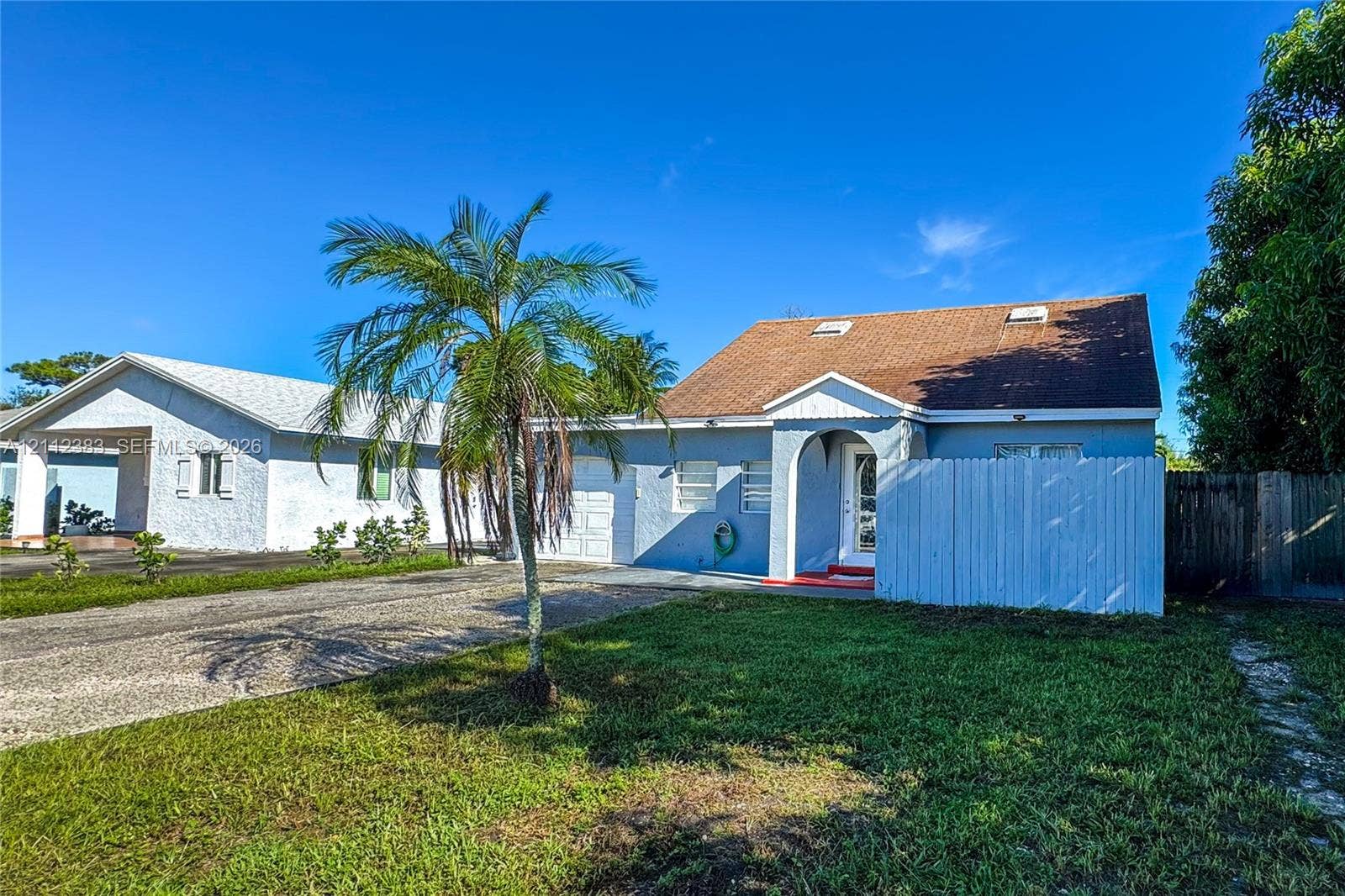 5319 Lake Boulevard, Delray Beach, Delray Beach, FL 33484 Single-story residence featuring a blue stucco exterior, gabled roof with skylights, an arched covered entryway, and a private wooden fence