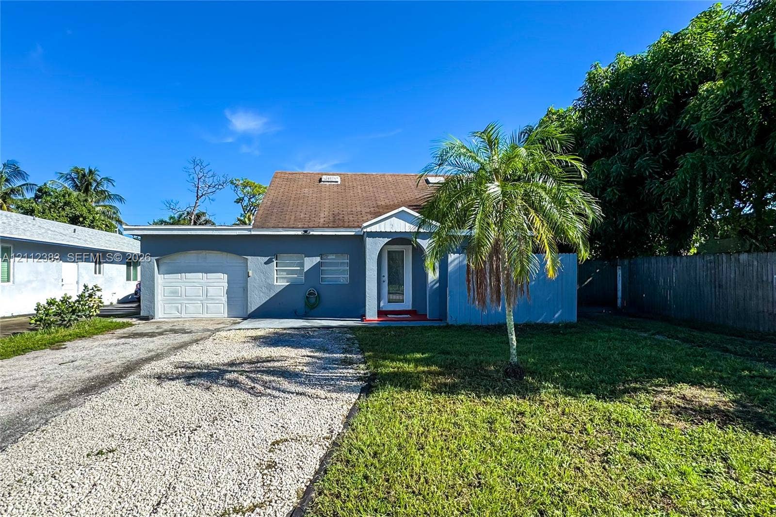 5319 Lake Boulevard, Delray Beach, Delray Beach, FL 33484 Single-story exterior featuring a shingled roof, attached one-car garage, gravel driveway, and arched entryway