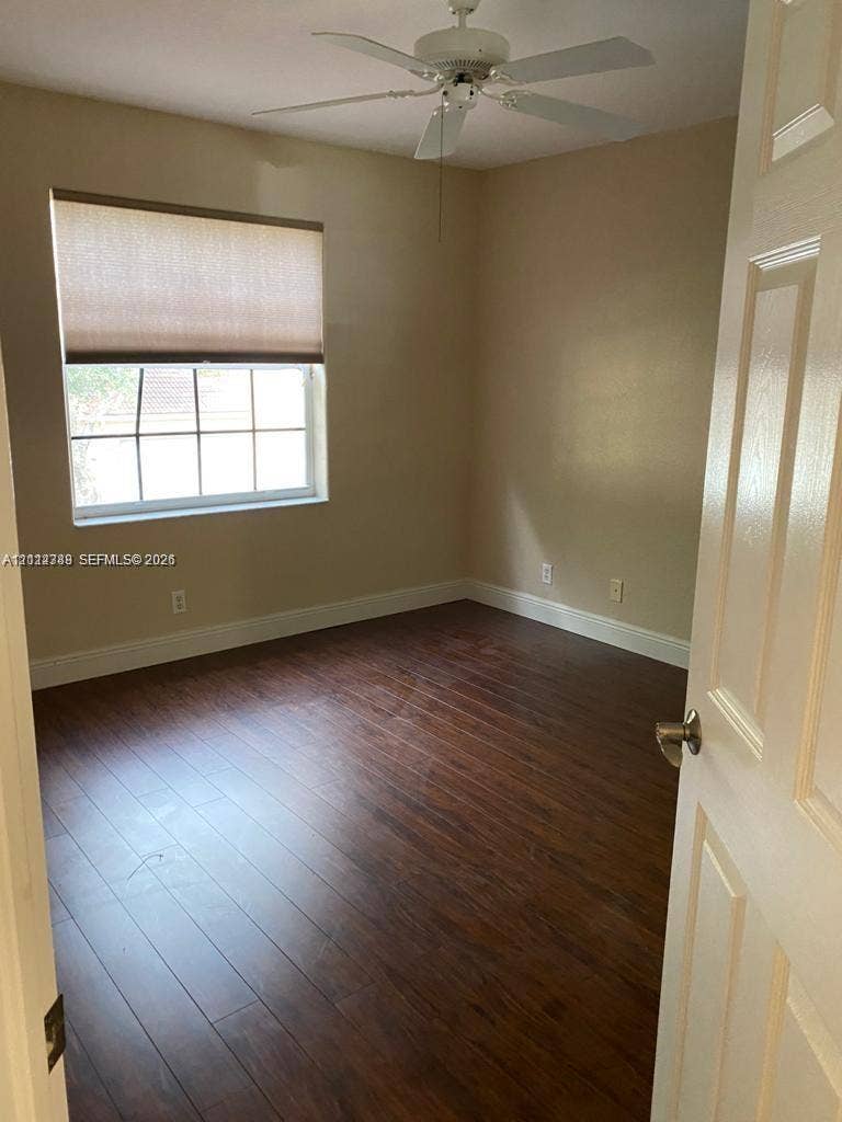 Interior room featuring wood-finish flooring, multi-pane window with custom roller shade, and ceiling-mounted fan with light fixture