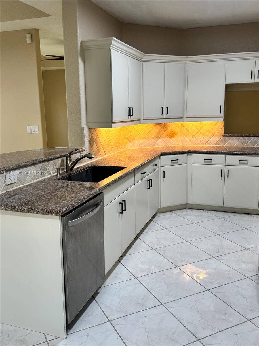 Kitchen featuring white cabinetry with matte black hardware, stone-finish countertops, tiled backsplash, and ceramic floor tiling
