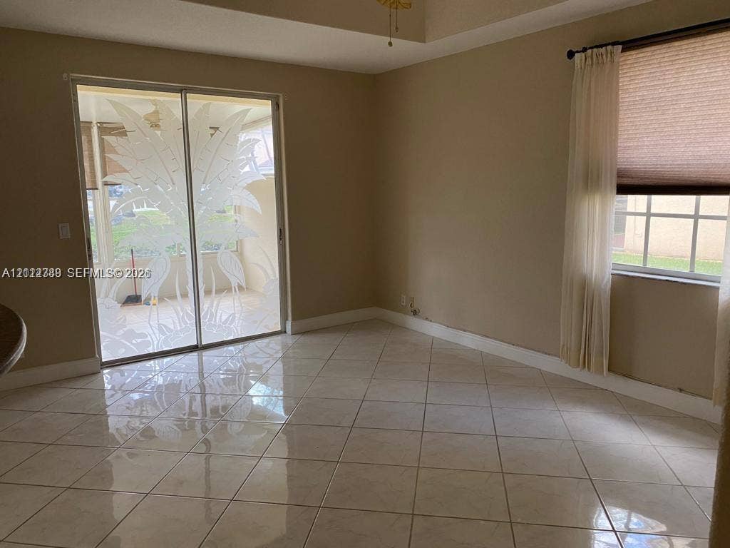 Interior space featuring polished ceramic tile flooring, a tray ceiling, and sliding glass doors with decorative etched glass