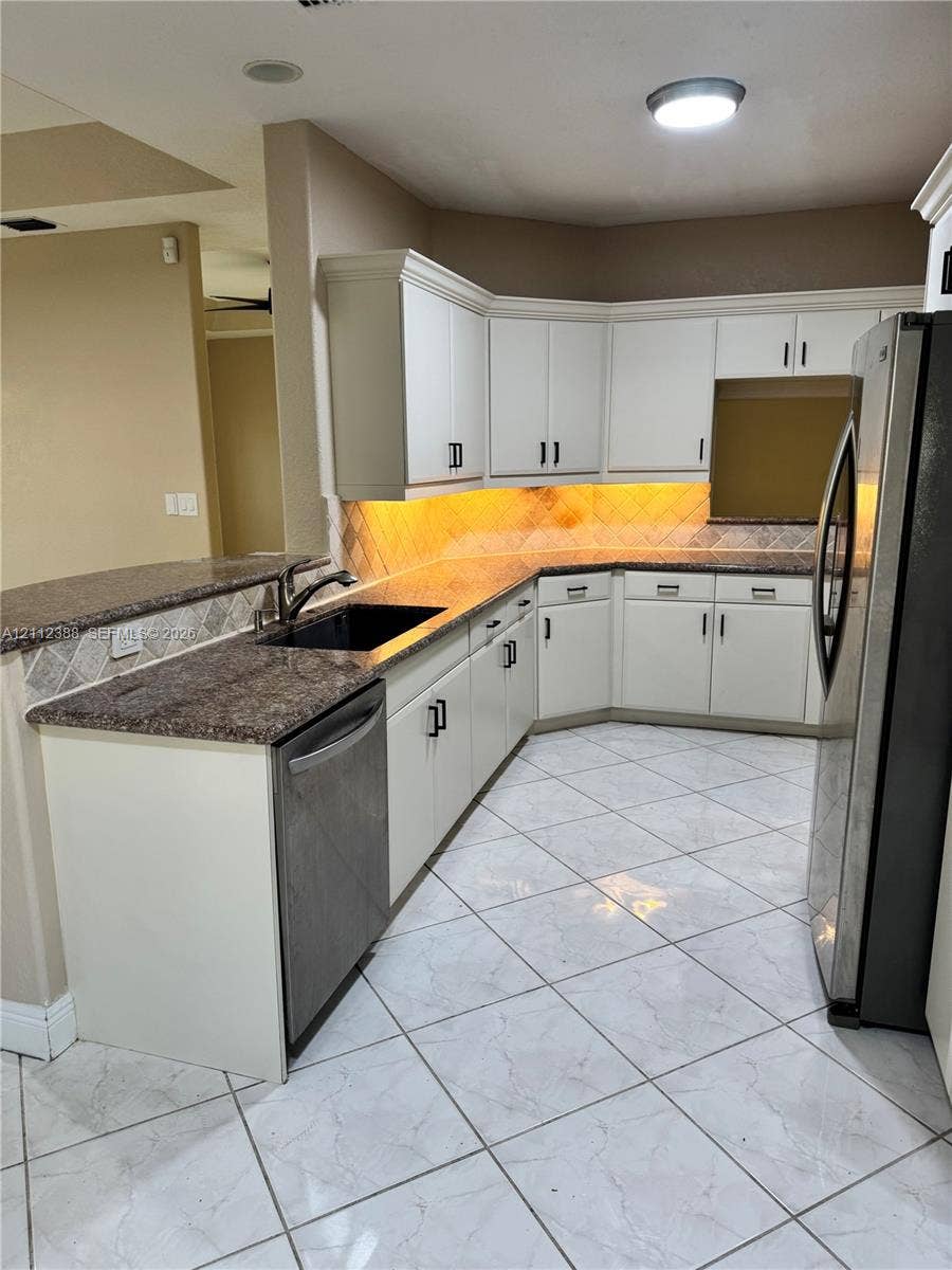 Kitchen featuring white cabinetry with matte black hardware, stone-finish countertops, tiled backsplash, and neutral-toned tile flooring