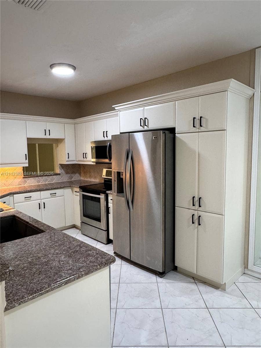 Kitchen featuring white shaker-style cabinetry with matte black hardware, stone-finish countertops, stainless steel appliances, and tile flooring