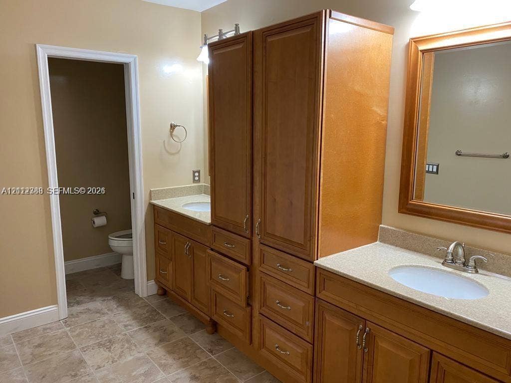 Double vanity featuring wood cabinetry, stone-finish countertops, dual drop-in sinks, and a built-in central storage tower with drawers