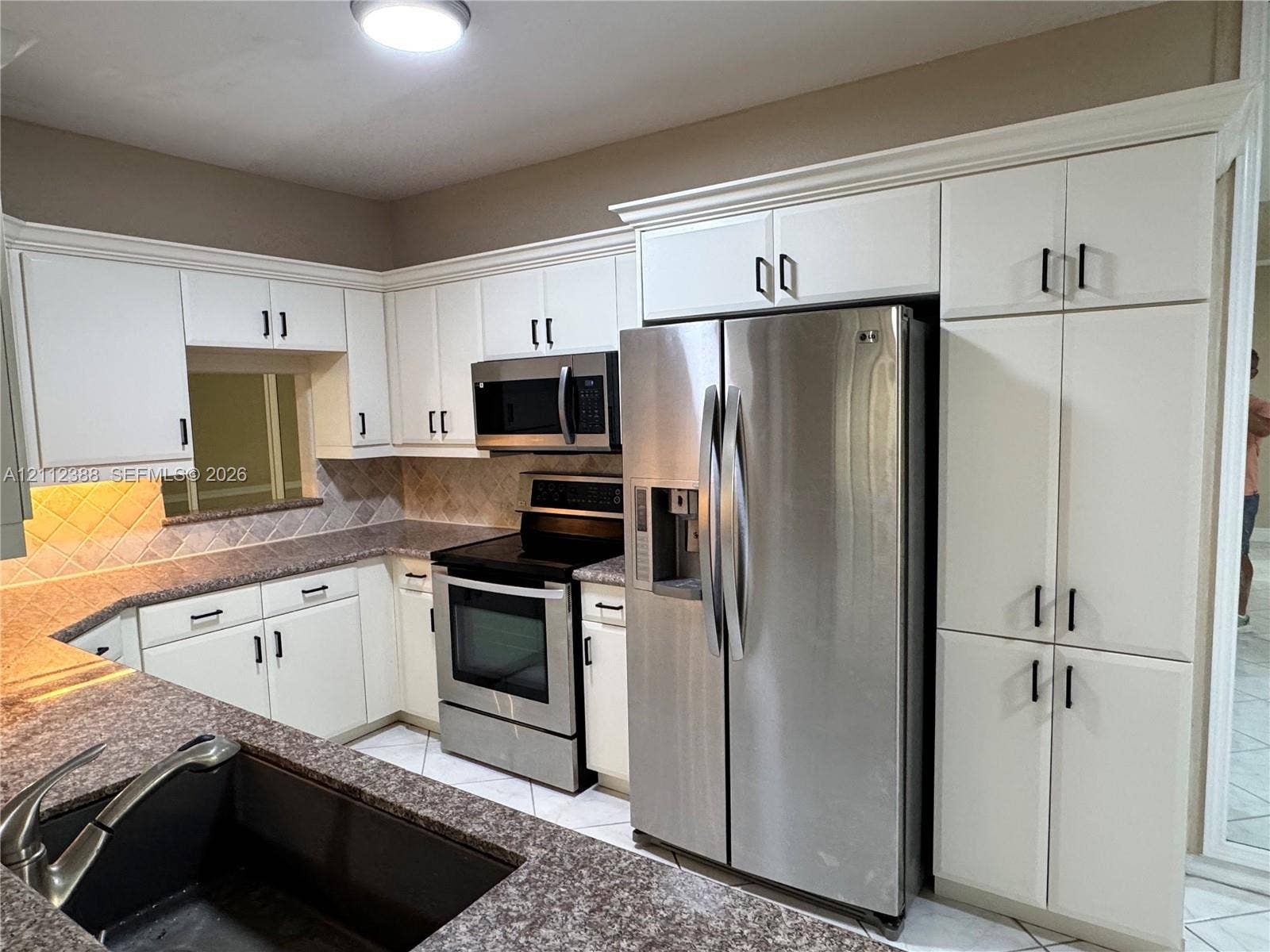 Kitchen featuring white cabinetry with crown molding, stone-finish countertops, stainless steel appliances, a tile backsplash, and a double-basin undermount sink
