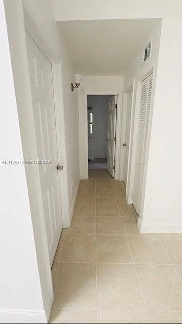 10765 Cleary Boulevard, #305, Plantation, Plantation, FL 33324 Hallway featuring neutral large-format tile flooring, multi-panel doors, white louvered closet doors, and wall-mounted sconce lighting