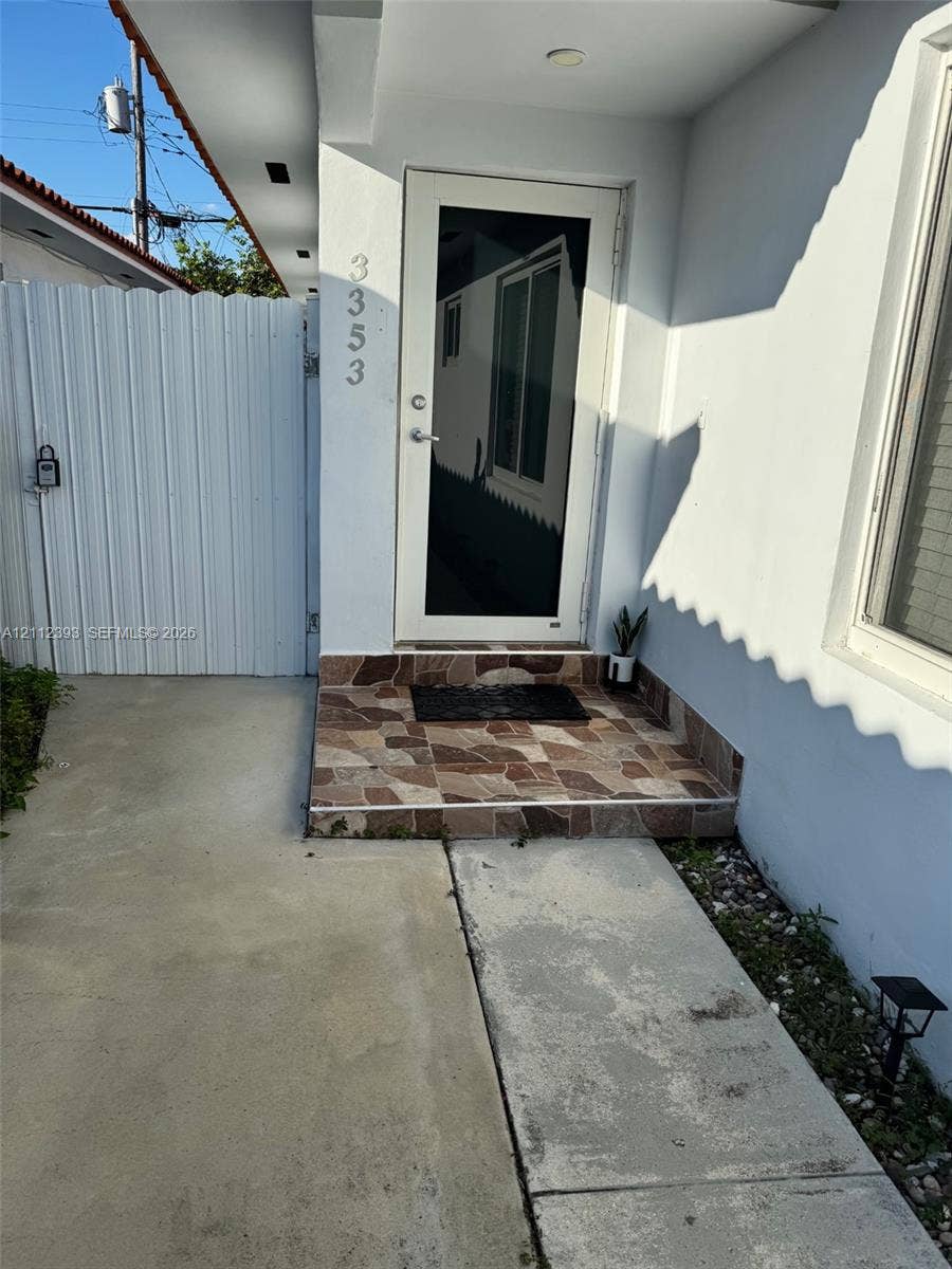 Entryway featuring a full-glass storm door, raised stone-finish landing, and white vertical privacy fencing