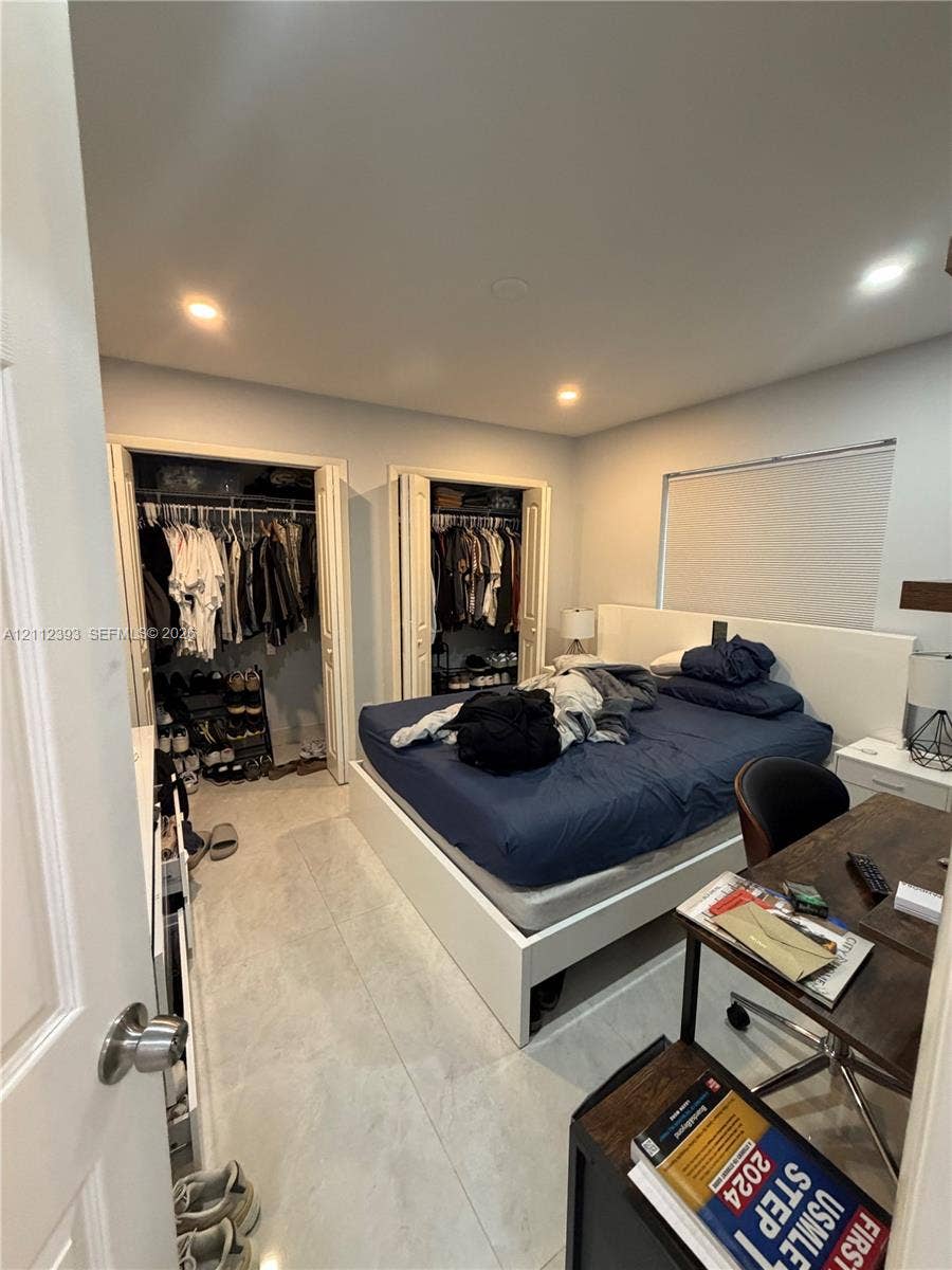Light-toned stone-finish tile flooring, recessed ceiling lighting, and dual closets with bi-fold doors