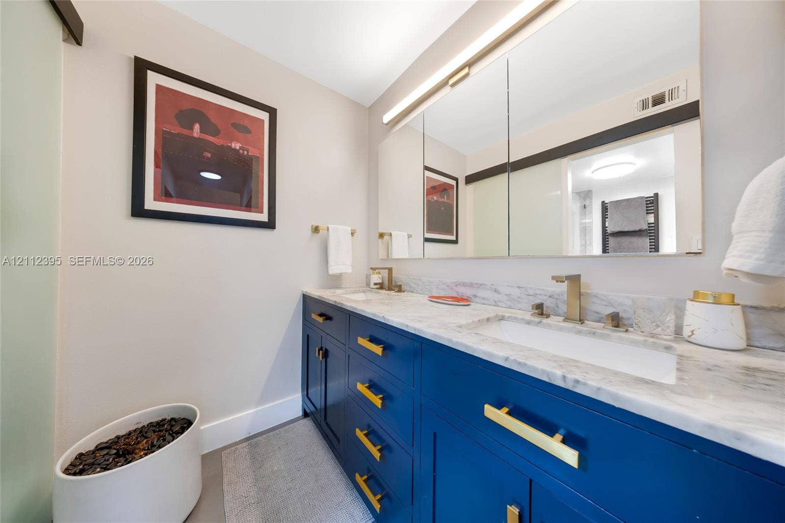 Dual-basin vanity featuring stone countertop, undermount sinks, gold-tone hardware, and built-in medicine cabinet with integrated lighting