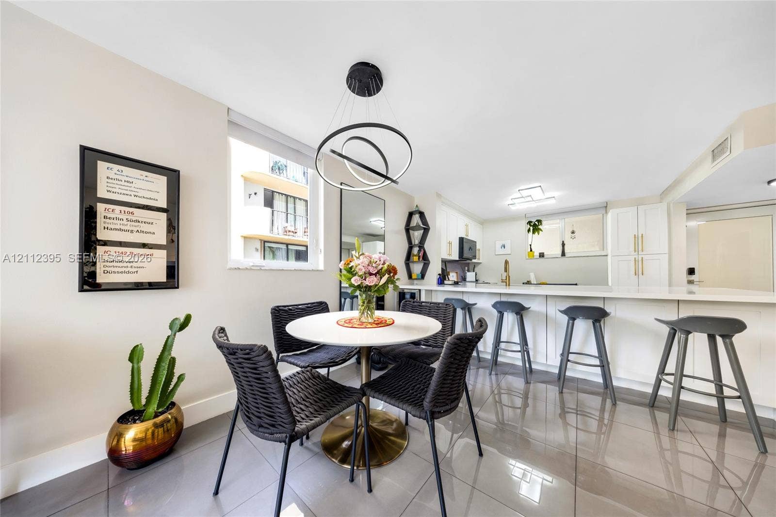 Open-concept kitchen and dining area featuring large-format tile flooring, white cabinetry with gold-tone hardware, a breakfast bar, and a modern tiered ring chandelier