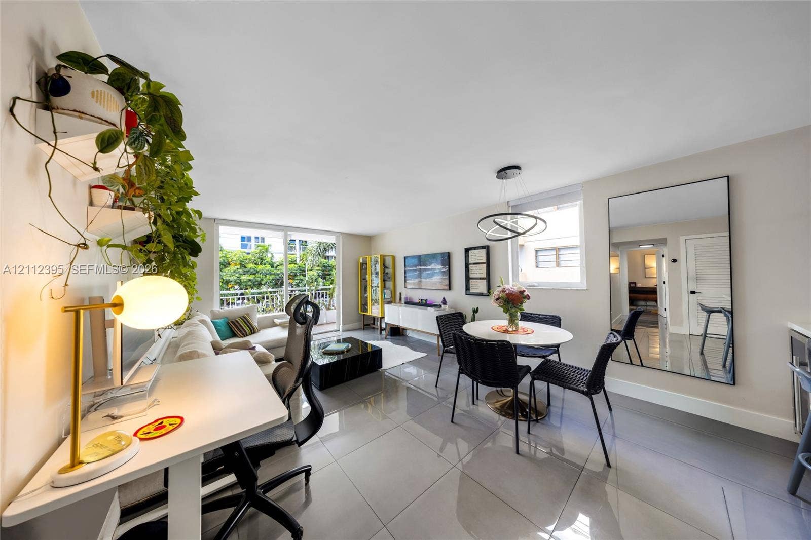 Open-concept living area featuring large-format tile flooring, a modern circular multi-ring chandelier, and floor-to-ceiling glass sliding doors opening to a balcony