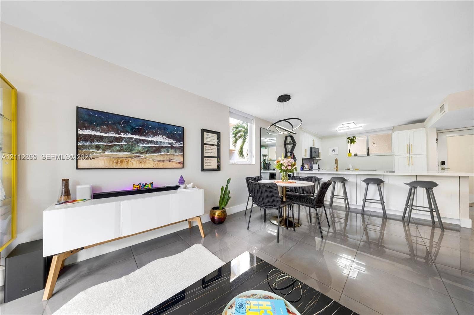 Open-concept interior featuring large-format tile flooring, recessed lighting, a modern multi-ring chandelier, and a kitchen island with integrated seating