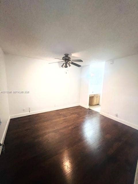 Interior space featuring dark wood-finish flooring, neutral wall tones, and a ceiling fan with integrated multi-bulb lighting fixture