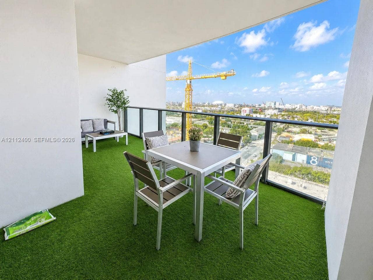 Covered balcony featuring synthetic turf flooring and a metal-framed glass railing