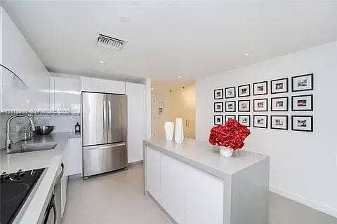 Modern kitchen featuring high-gloss cabinetry, a central island with a solid surface countertop, stainless steel appliances, and a polished sink with a curved faucet