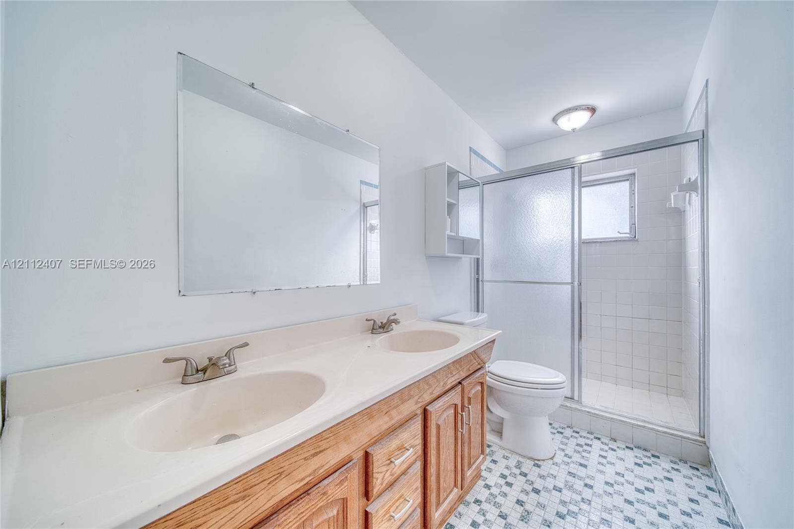 18520 SW 88th Road, Cutler Bay, FL 33157 Dual-sink vanity with a molded countertop, wood-finish cabinetry, frameless wall-mounted mirror, and walk-in shower with a glass enclosure