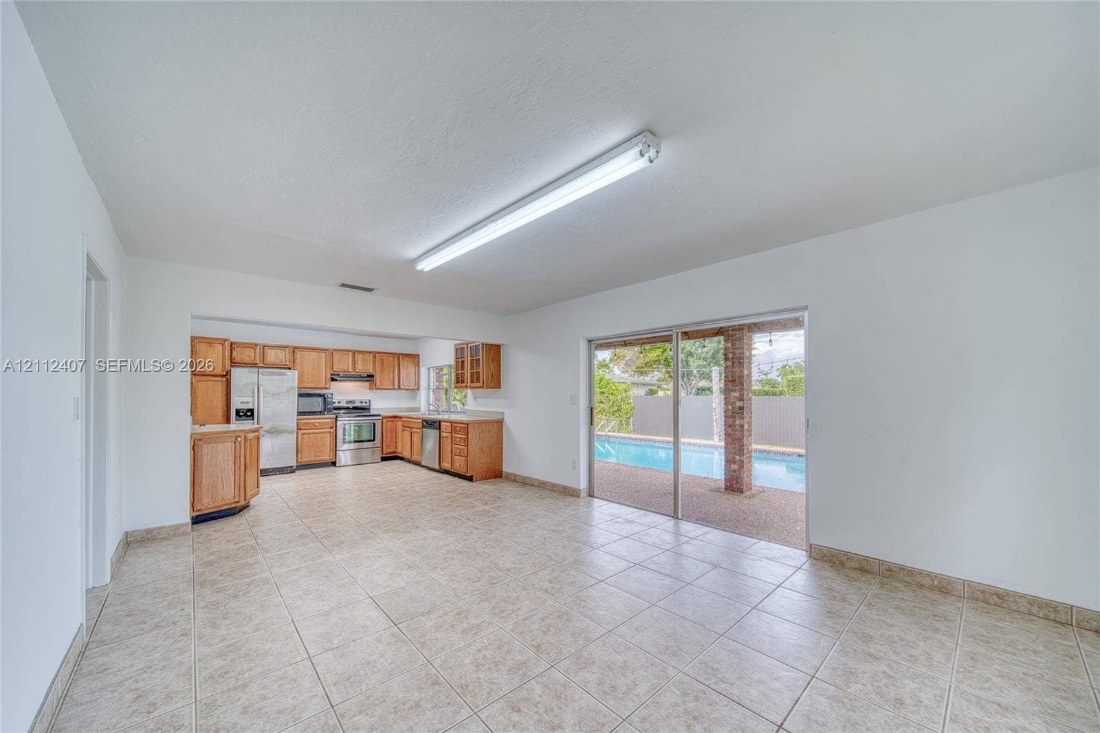 18520 SW 88th Road, Cutler Bay, FL 33157 Kitchen area featuring wood cabinetry, stainless steel appliances, and tile flooring, with sliding glass doors opening to a pool and covered patio