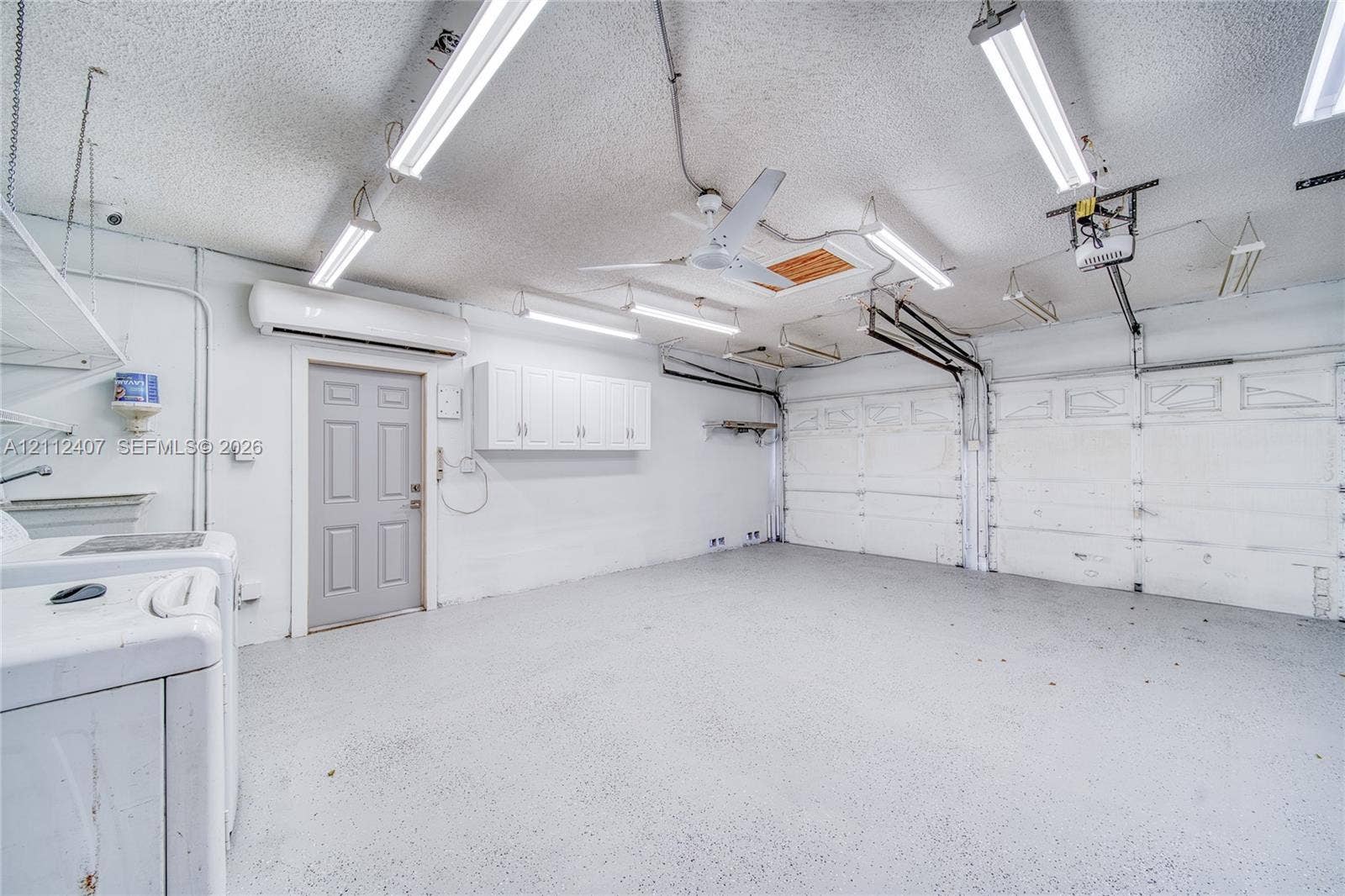 18520 SW 88th Road, Cutler Bay, FL 33157 Garage interior featuring epoxy-coated flooring, wall-mounted cabinetry, a ceiling-mounted fan, overhead fluorescent lighting, and a climate-control unit