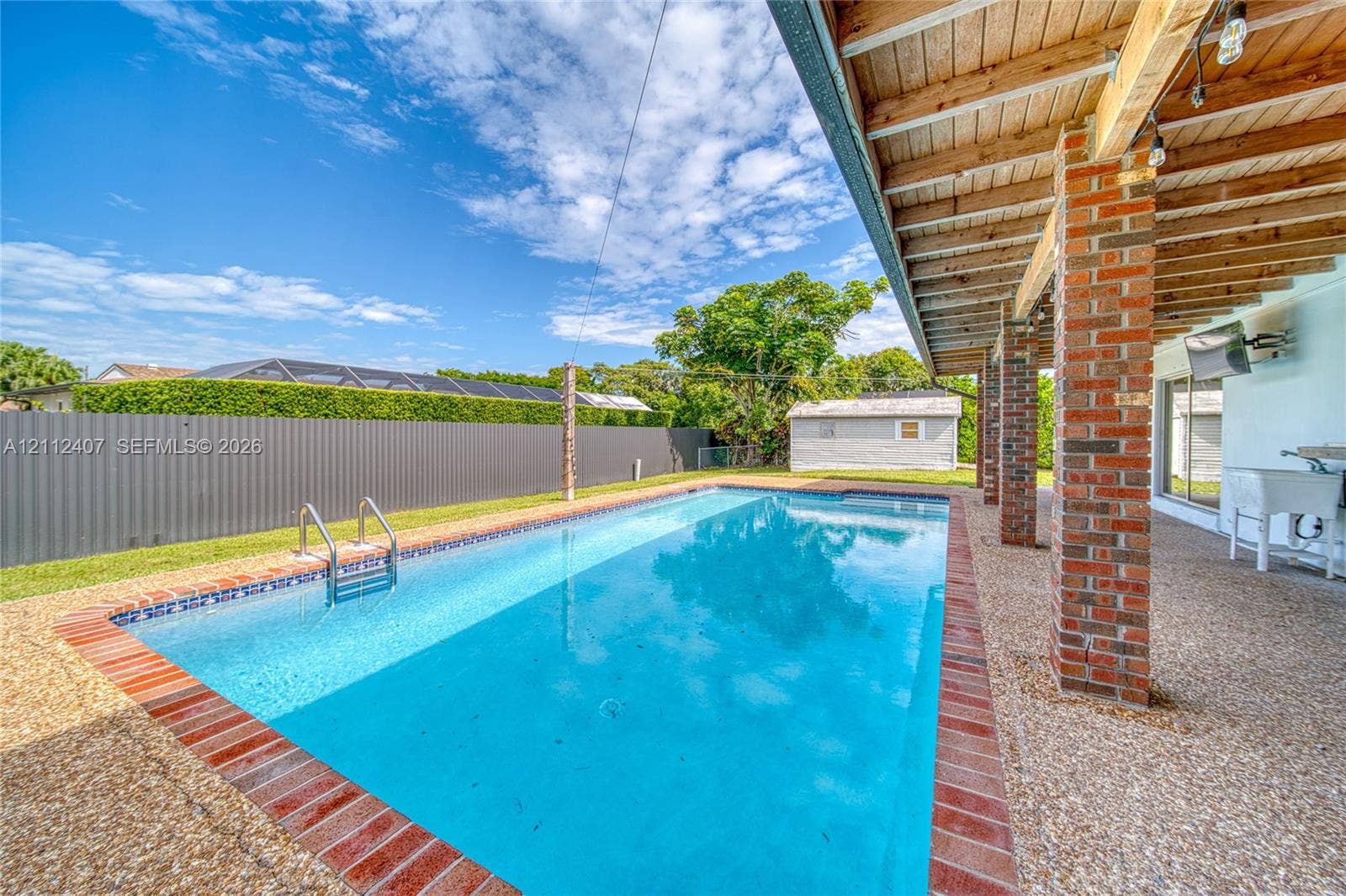 18520 SW 88th Road, Cutler Bay, FL 33157 Rectangular in-ground swimming pool featuring a brick surround, covered patio with exposed wood ceiling beams, exposed brick structural pillars, and a metal privacy fence