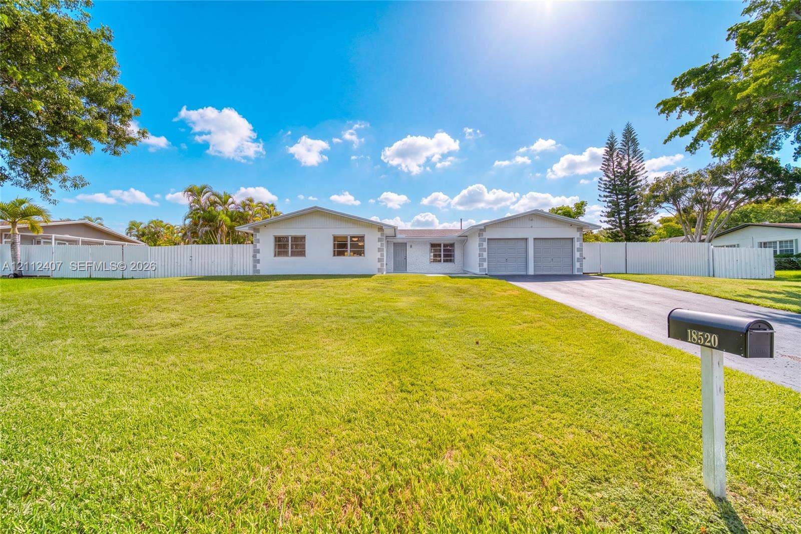 18520 SW 88th Road, Cutler Bay, FL 33157 Single-story exterior featuring a painted masonry facade, two-car garage, asphalt driveway, and full perimeter vinyl fencing on a grass lot