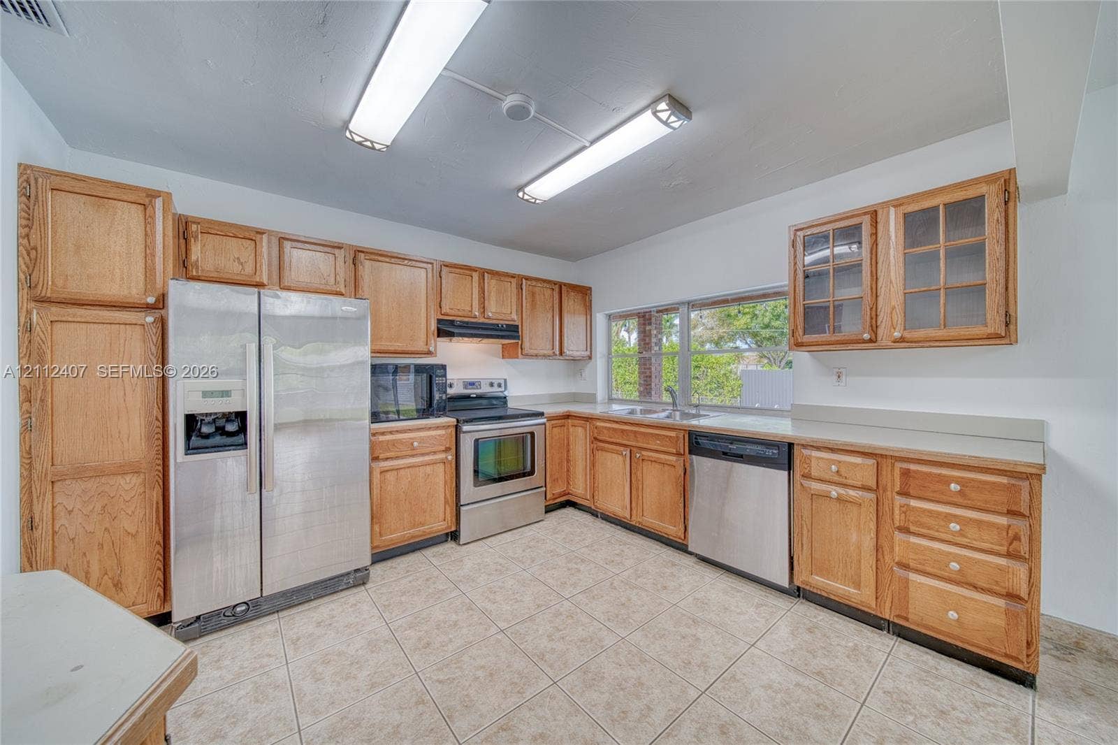 18520 SW 88th Road, Cutler Bay, FL 33157 Kitchen featuring medium-tone wood cabinetry, solid-surface countertops, tile flooring, and a stainless steel appliance package including a refrigerator, dishwasher, and electric range