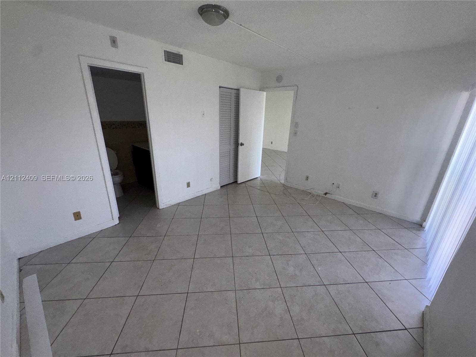 Interior space featuring neutral tile flooring, louvered closet doors, and flush-mount lighting