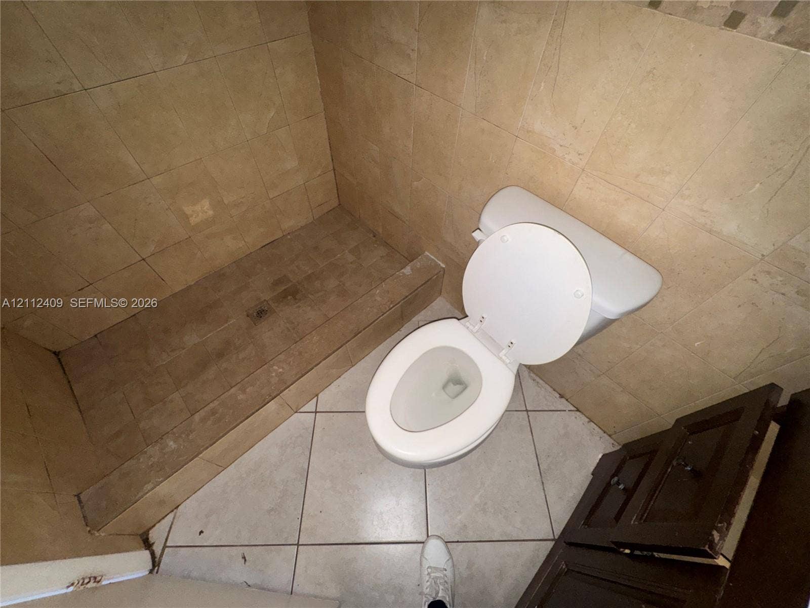 Shower area featuring tiled walls and flooring, accompanied by a toilet and a dark wood-finish vanity cabinet