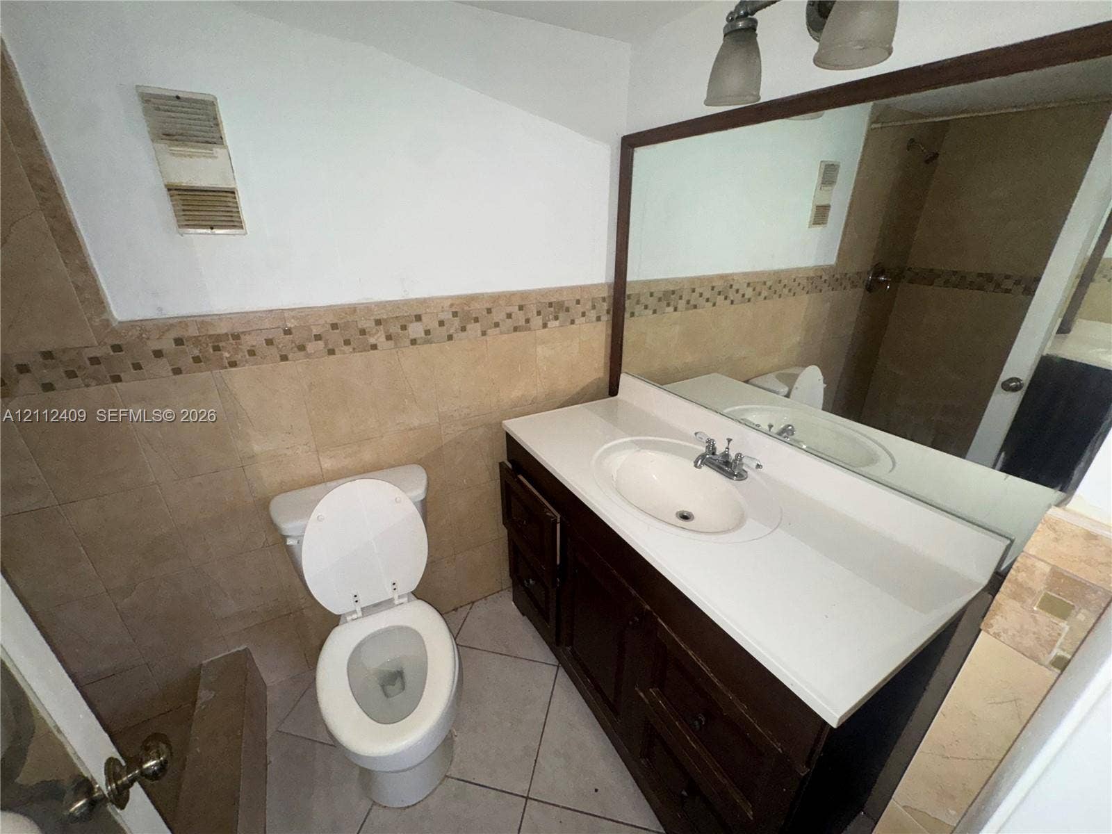 Bathroom featuring a dark wood-finish vanity with a white countertop and oval under-mount sink, tiled walls with a mosaic accent border, and ceramic tile flooring
