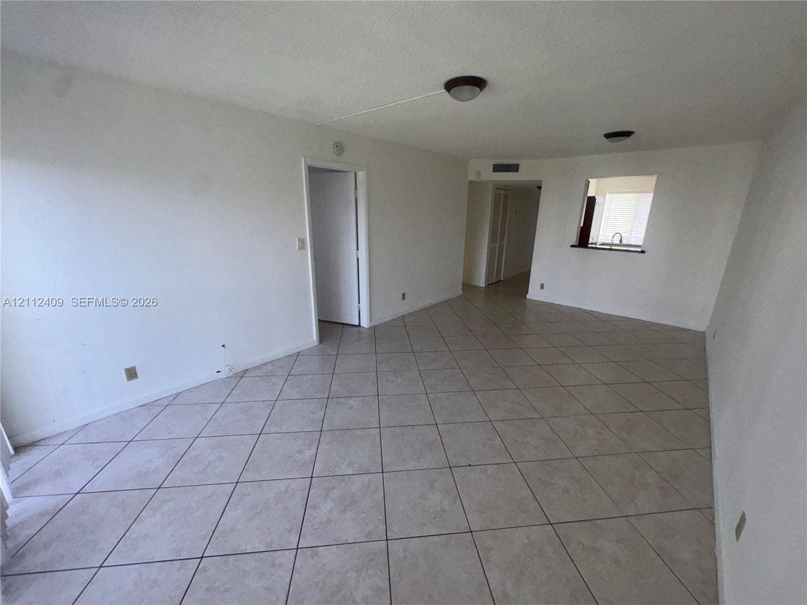 Open-concept interior featuring neutral tile flooring, flush-mount ceiling lighting, and a kitchen passthrough window