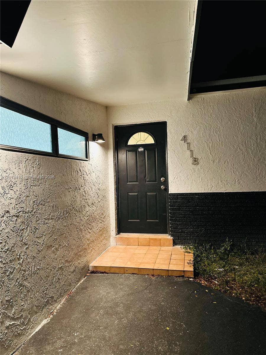 Covered entryway featuring a textured stucco facade, a black six-panel entry door with a semi-circular transom window, and a tiled stoop