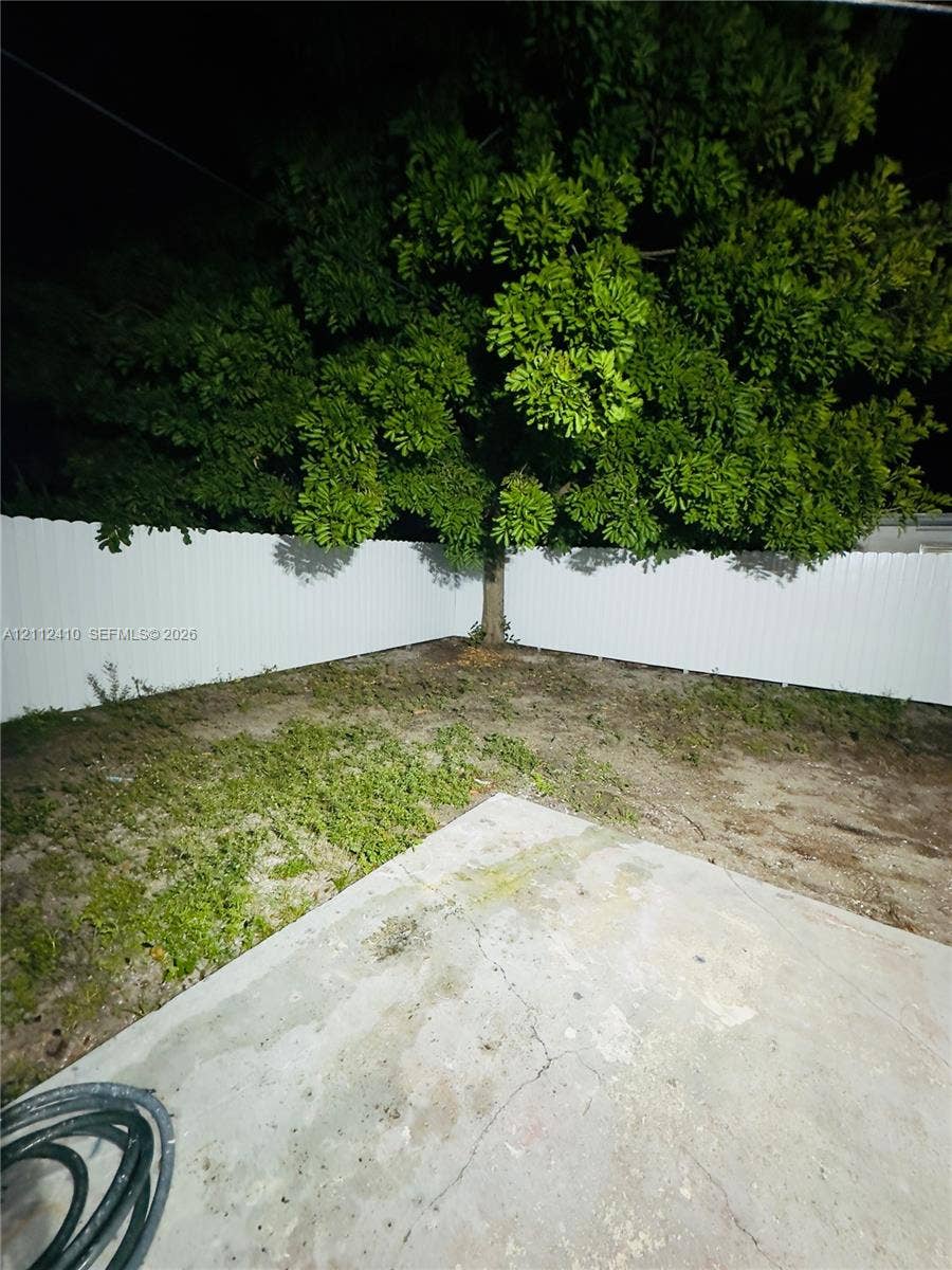 Backyard featuring a concrete patio, white vinyl fencing, and a mature tree