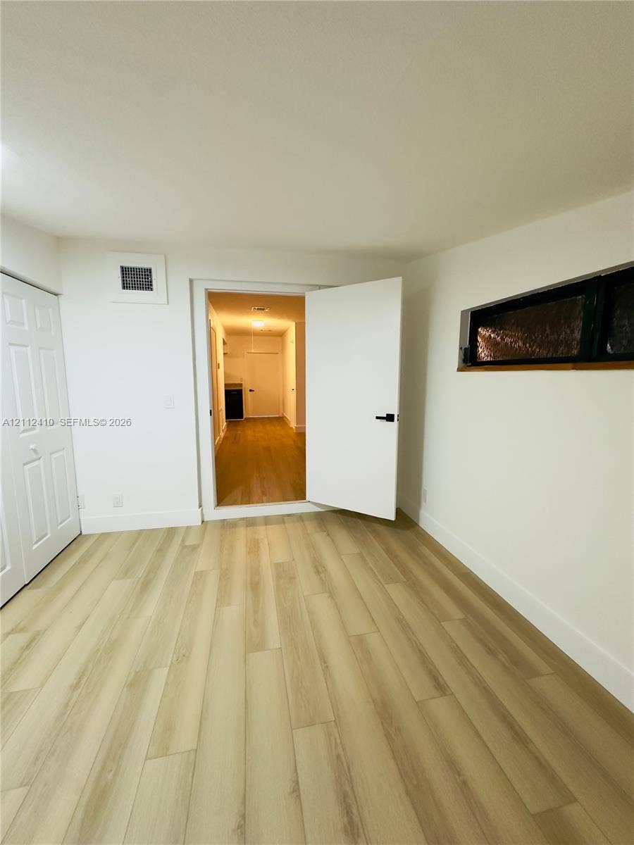 Room featuring wood-finish flooring, a white paneled closet door, a rectangular horizontal window with dark framing, and a white interior door with matte black hardware