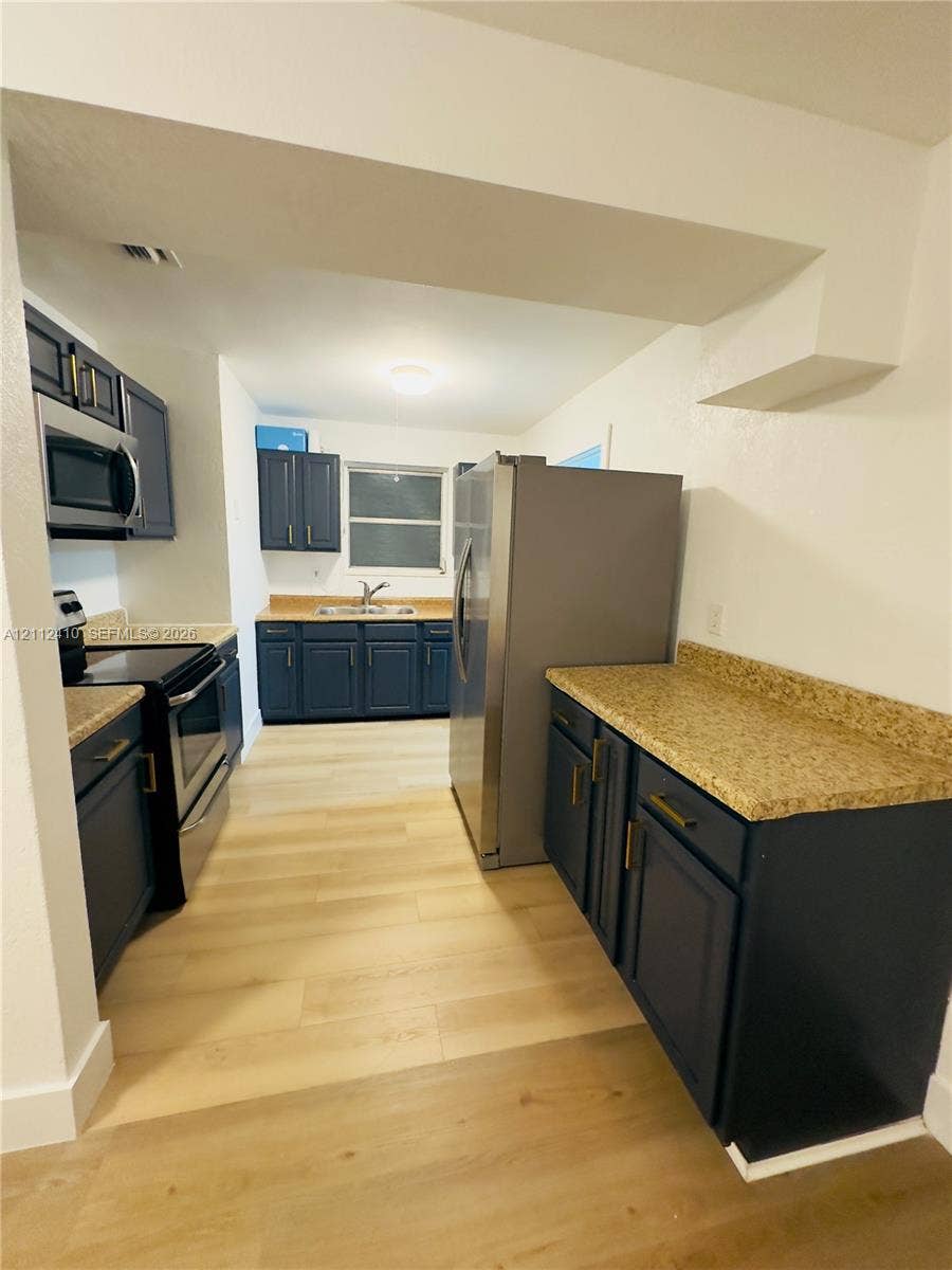 Kitchen featuring navy shaker-style cabinetry, stone-finish countertops, wood-finish flooring, and stainless steel appliances