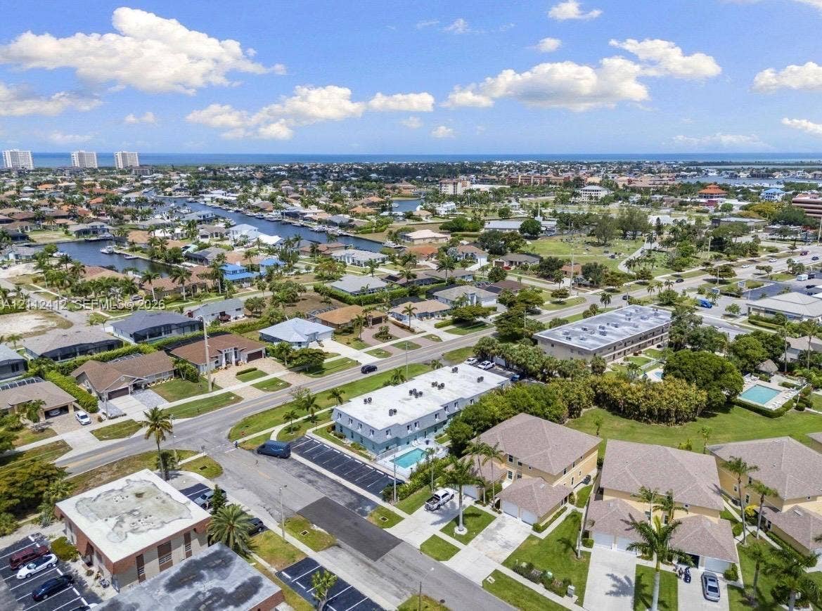 Aerial perspective of coastal residential area featuring waterfront access, proximity to regional waterways, palm tree landscaping, and paved parking lots