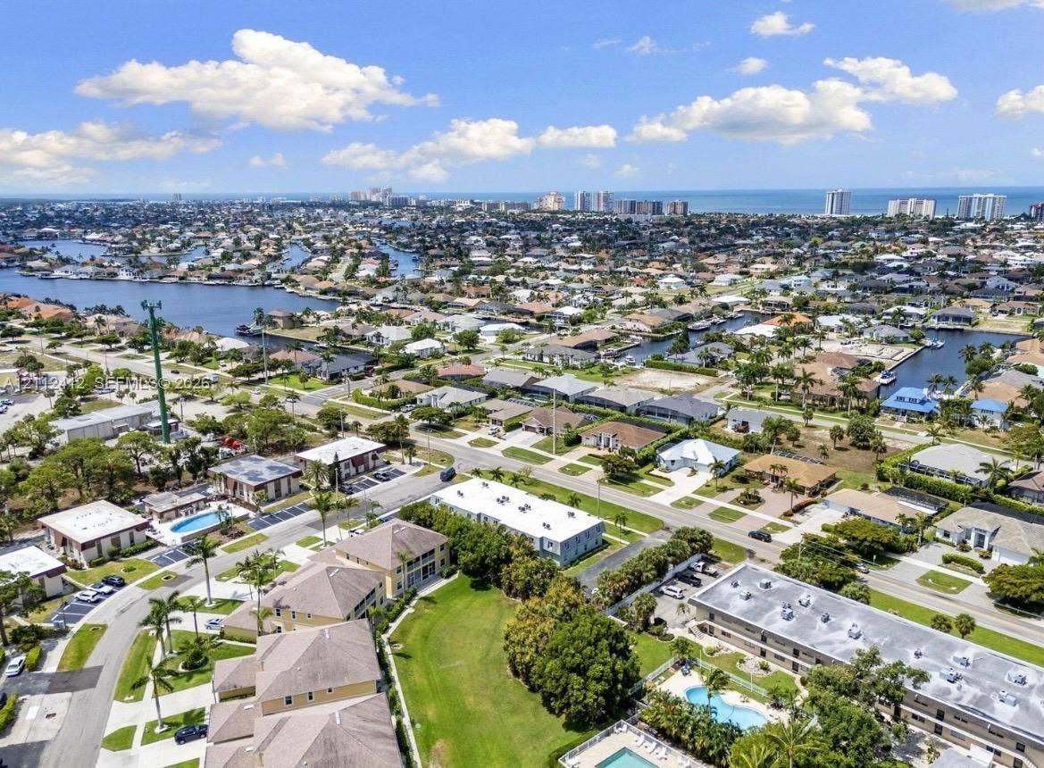 Aerial perspective of coastal residential area featuring waterfront canals, mature landscaping, community swimming pools, and proximity to the ocean