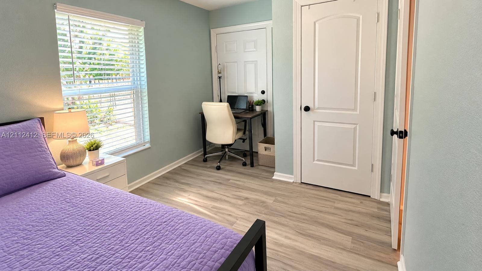 Room with wood-finish flooring, light-toned wall paint, a window with integrated blinds, and two interior doors featuring matte black hardware