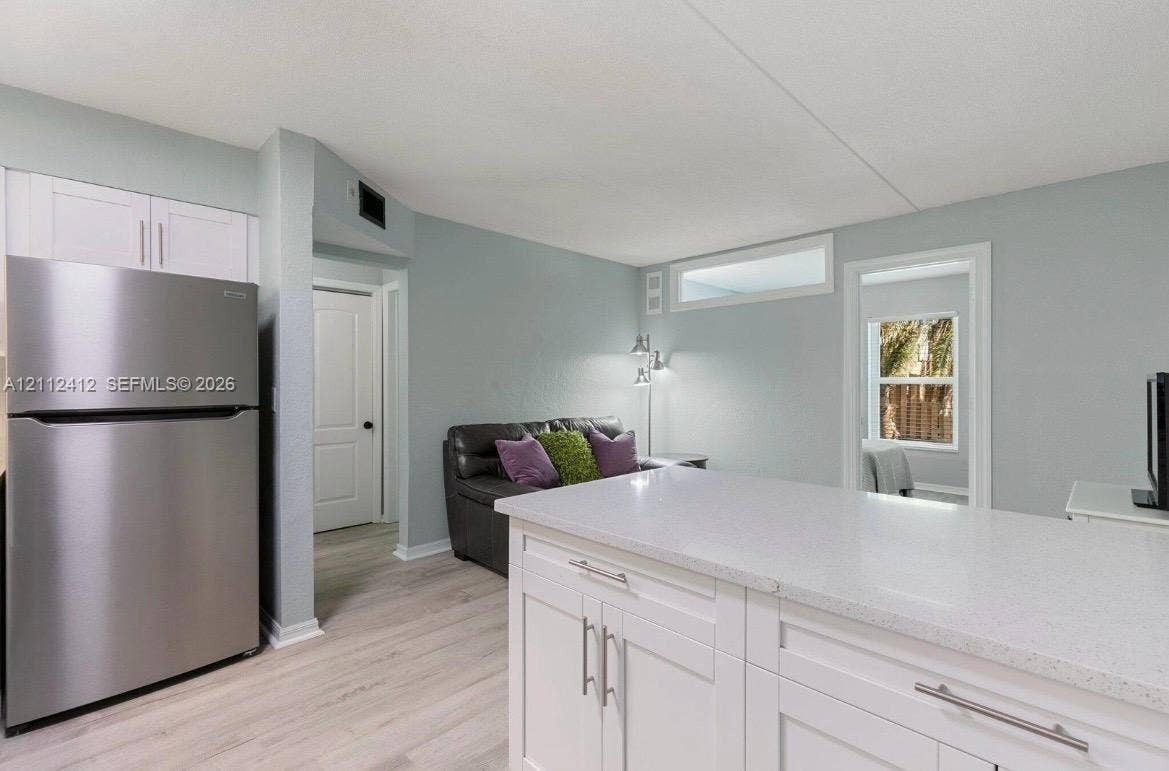 Kitchen area featuring white cabinetry, a quartz countertop island, stainless steel refrigerator, and wood-finish flooring