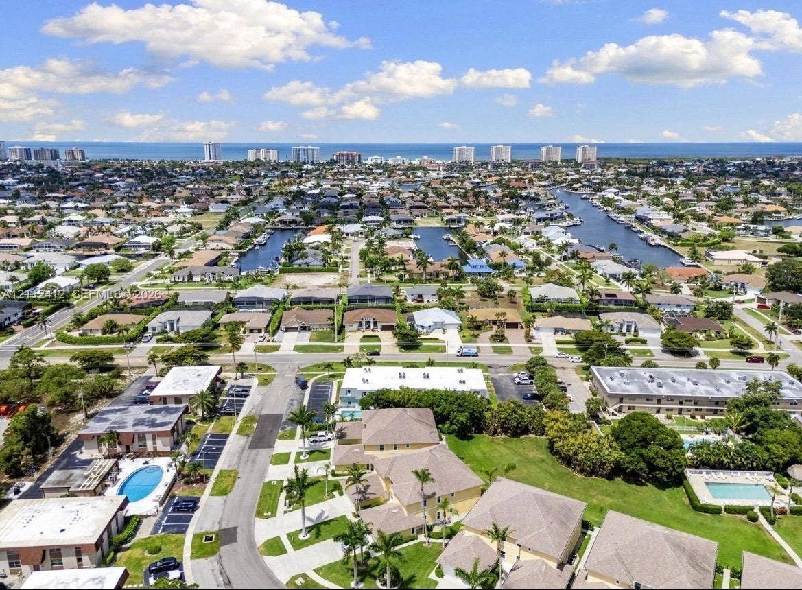 Aerial perspective of a coastal community featuring paved residential streets, expansive green spaces, mature palm trees, and proximity to the open ocean