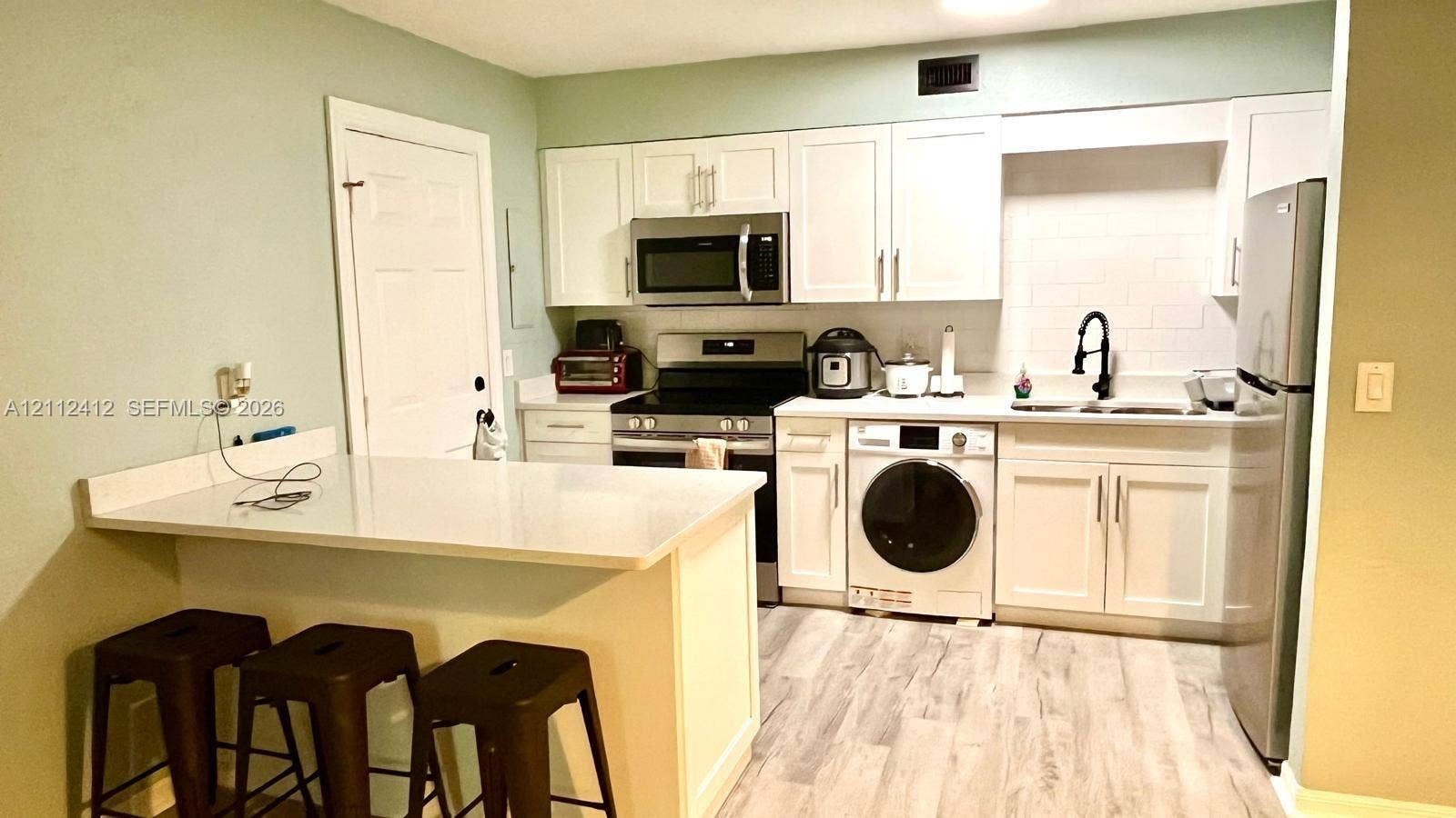 Kitchen featuring white cabinetry, wood-finish flooring, a quartz countertop peninsula, stainless steel appliances, and a matte black faucet