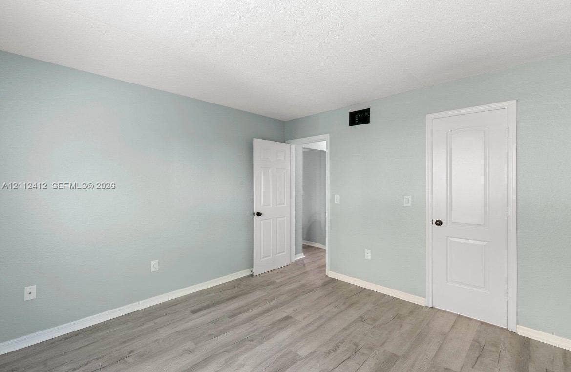 Room featuring neutral-toned walls, wood-finish flooring, and white two-panel interior doors with matte black hardware