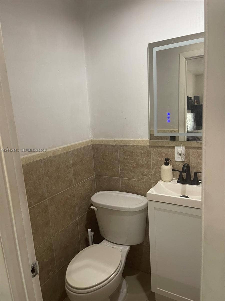 10830 Westwood Lake Drive, #0, Miami, Miami, FL 33165 Wall-mounted LED backlit mirror, pedestal-style vanity with a rectangular sink, matte black faucet, and tiled wainscoting