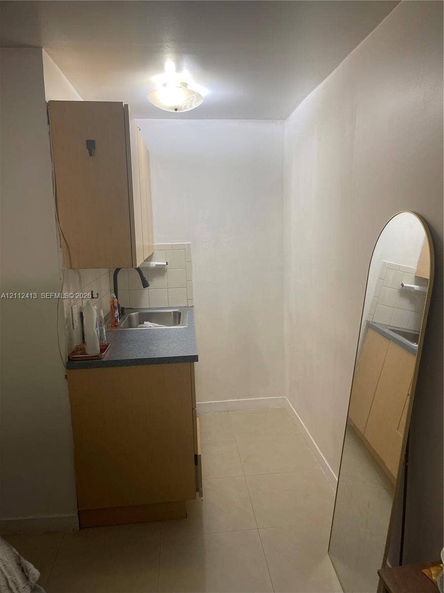 10830 Westwood Lake Drive, #0, Miami, Miami, FL 33165 Compact kitchenette featuring light-finish cabinetry, a neutral solid-surface countertop, stainless steel drop-in sink, tile backsplash, and ceramic floor tiling
