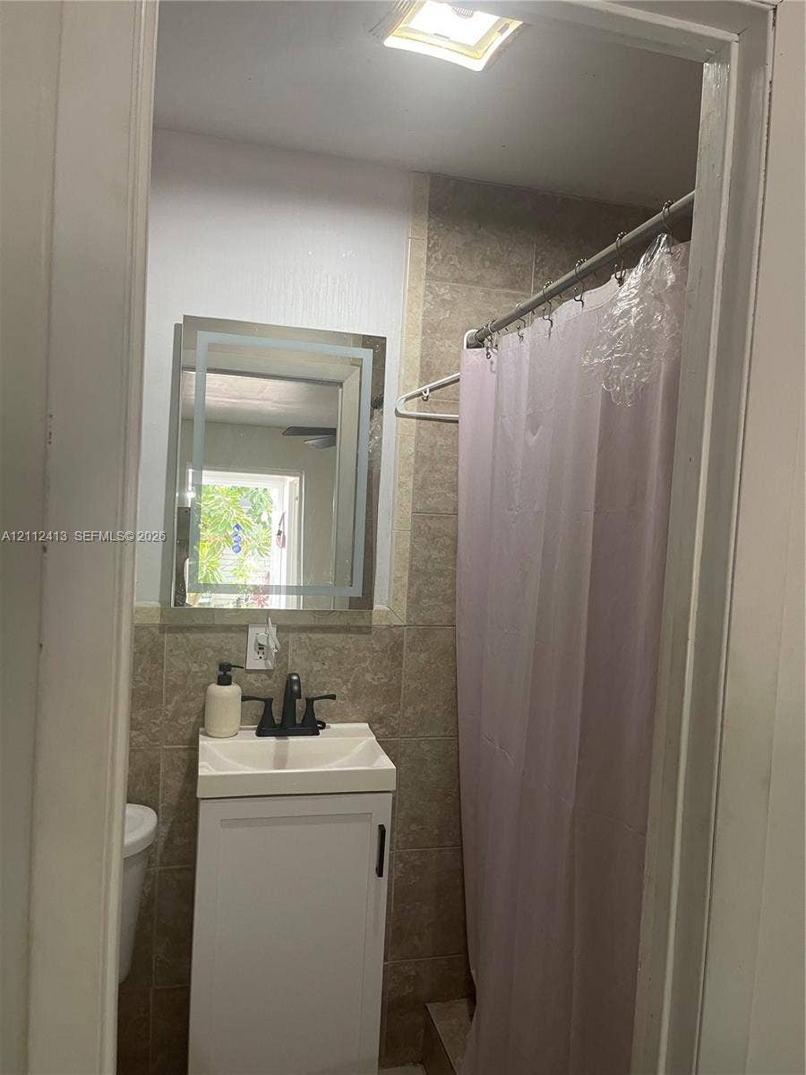 10830 Westwood Lake Drive, #0, Miami, Miami, FL 33165 Bathroom featuring a vanity with a white basin, matte black faucet, illuminated wall mirror, and tile-surround shower area