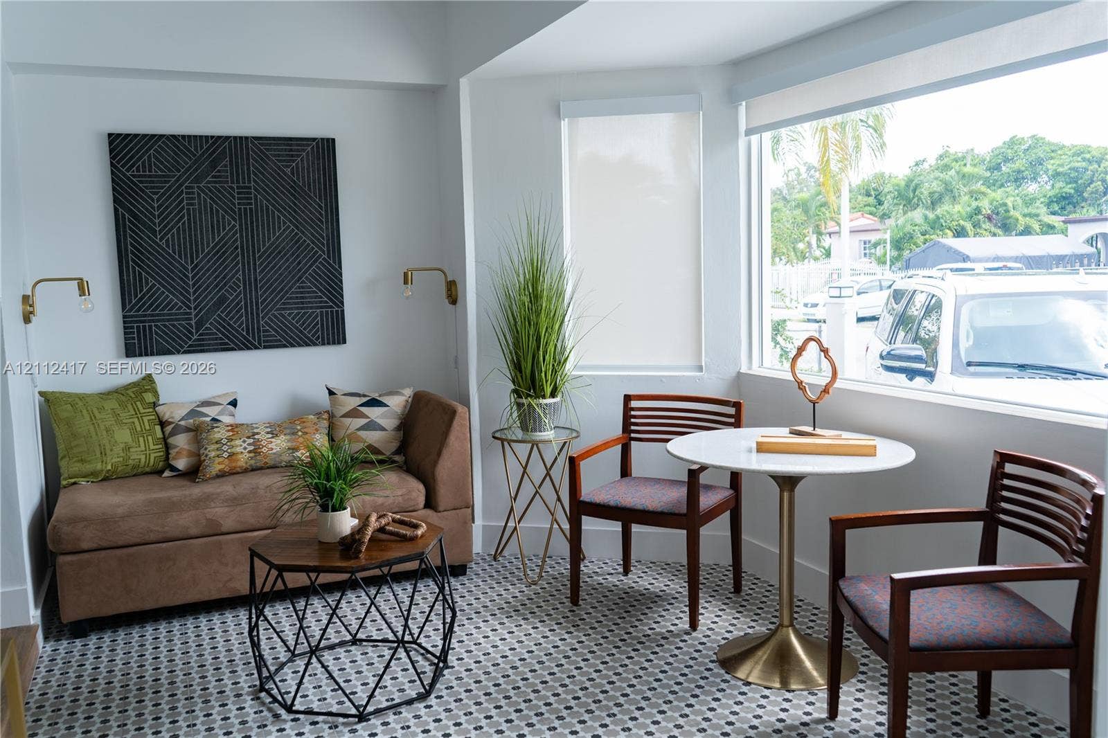 Large bay window, neutral wall color, and wall-mounted brass light fixtures