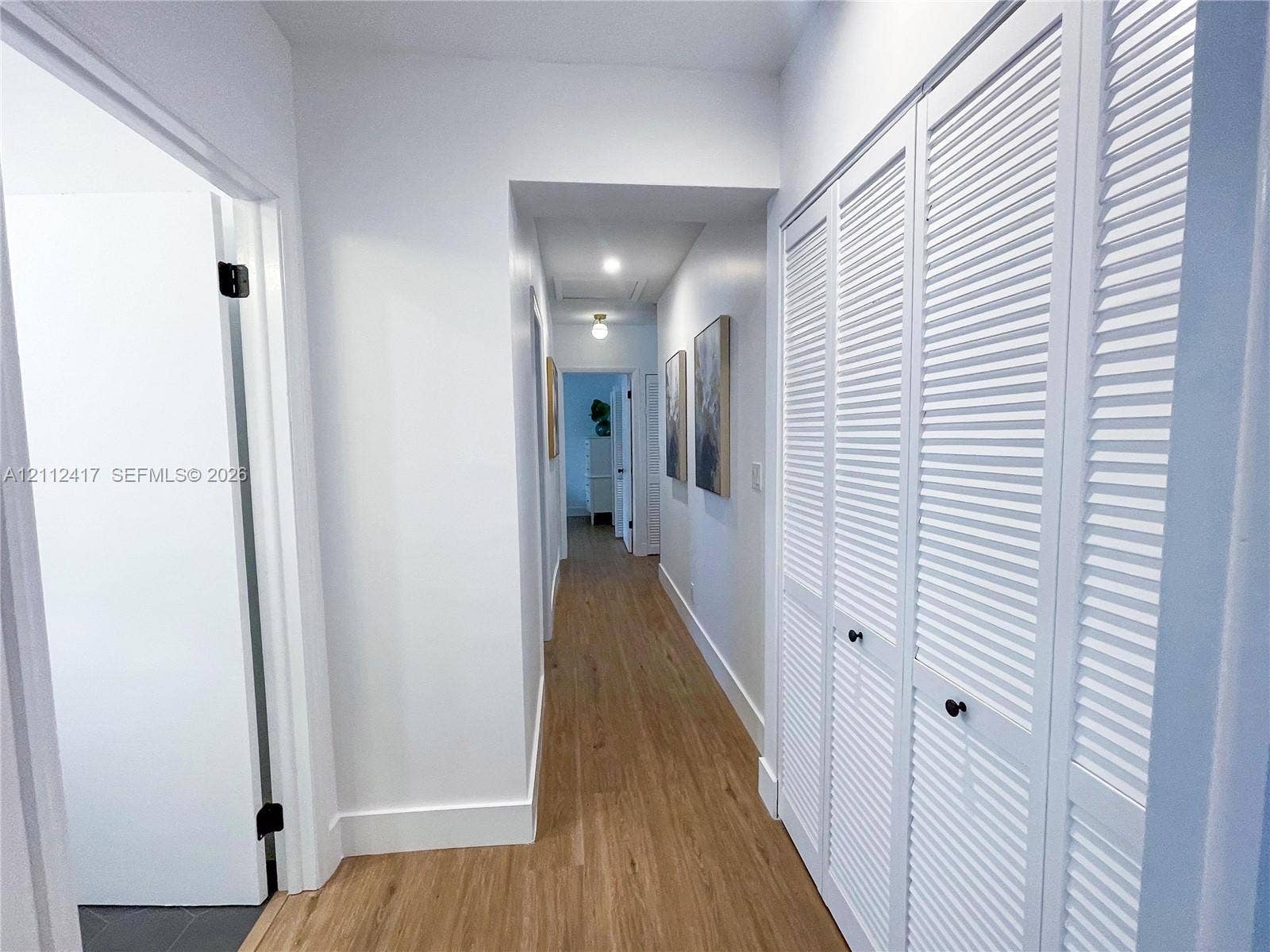 Hallway featuring wood-finish flooring, white louvered closet doors with matte black hardware, and recessed lighting