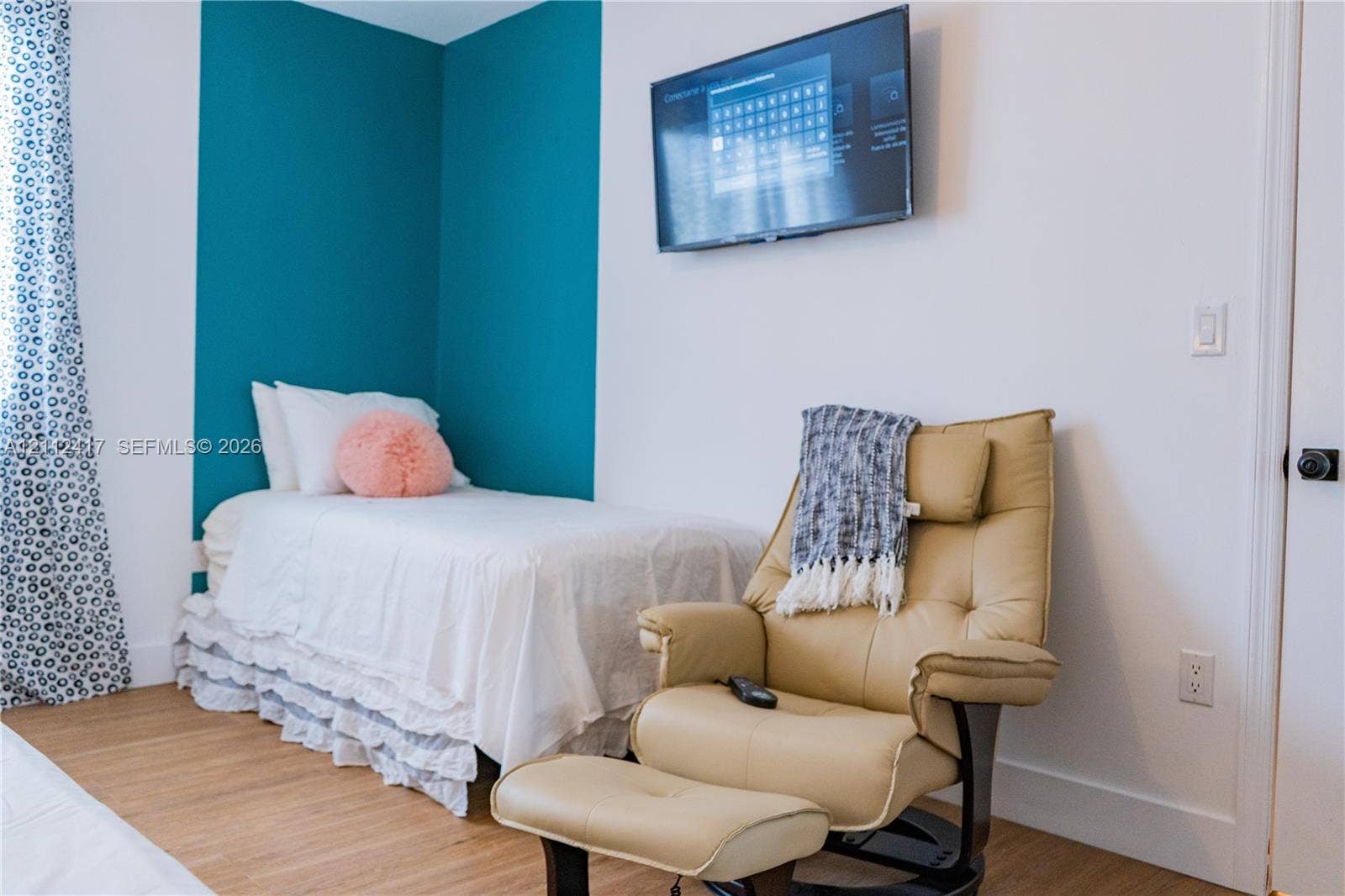Room featuring wood-finish flooring, a wall-mounted television, and a teal accent wall