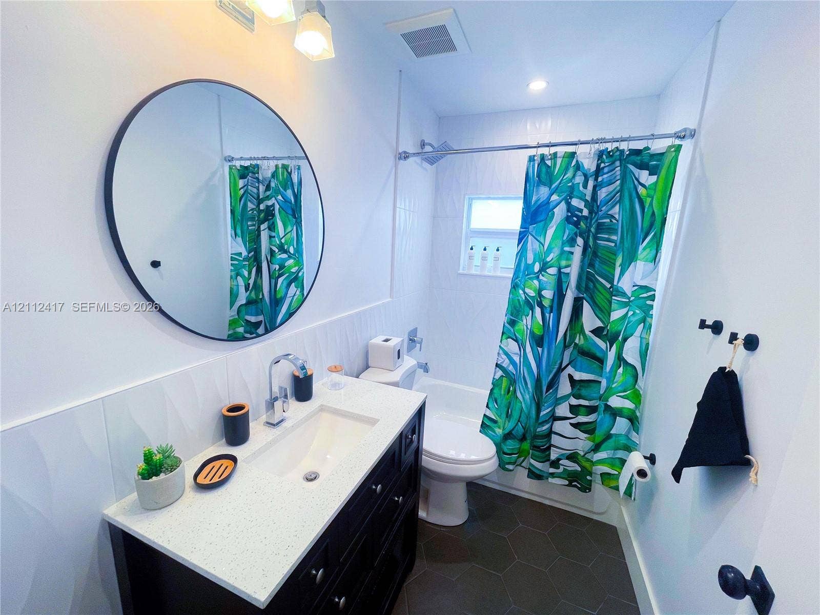 Bathroom featuring a dark wood-finish vanity with a stone countertop, an integrated rectangular sink, a circular mirror, and hexagonal floor tile