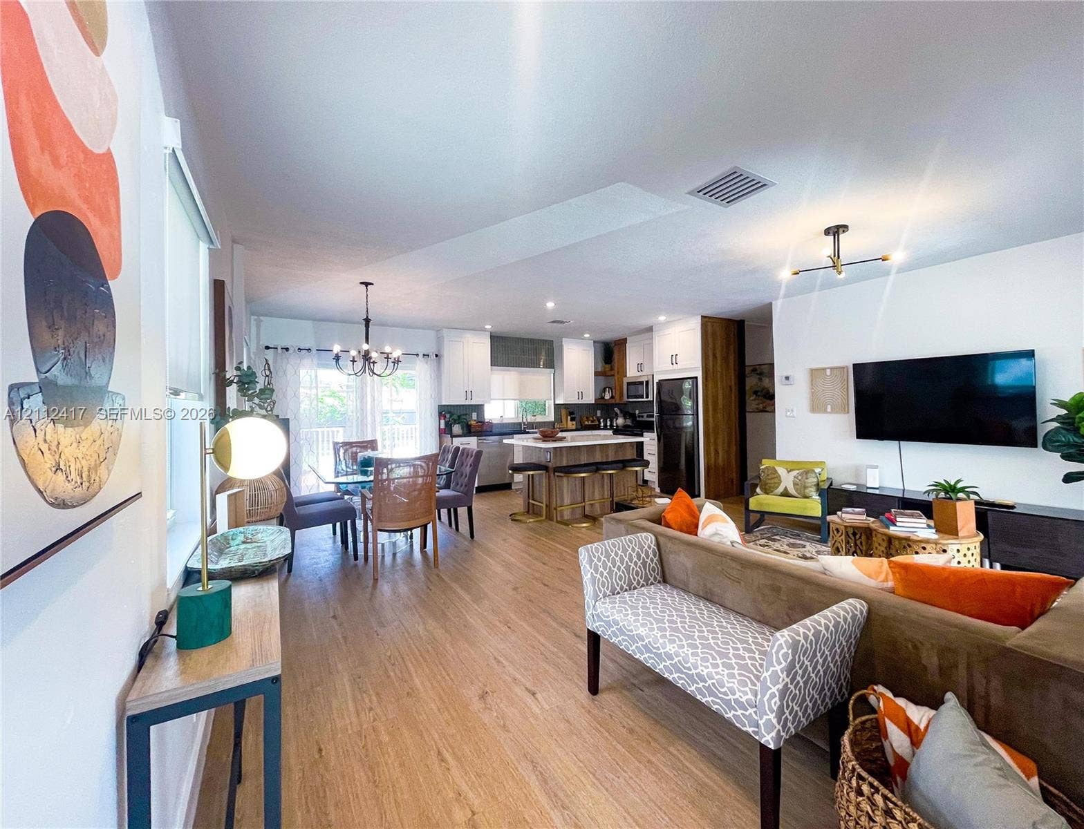 Open-concept interior featuring wood-finish flooring, white cabinetry, a center island with bar seating, and contemporary multi-arm overhead lighting
