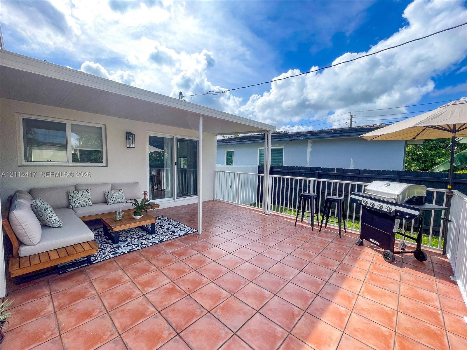 Covered patio featuring tiled flooring, sliding glass door access, and white metal perimeter fencing